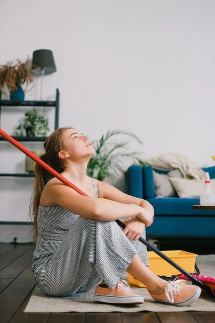 Two women in red overalls vacuuming and sweeping a modern living room.